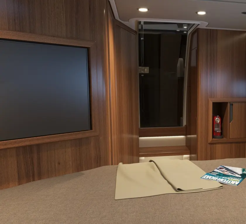 Modern cabin interior featuring a wall-mounted TV, wooden paneling, a beige blanket on the bed, and a magazine titled "Motor Boat.